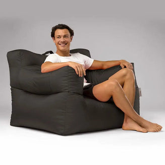 Man sitting on a large black bean bag chair against a gray background