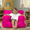 Child sitting on a bright pink bean bag chair in a colorful room with toys and books.