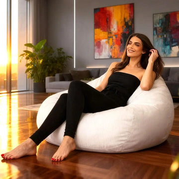 Woman sitting on a white bean bag chair in a modern living room with abstract art on the wall.