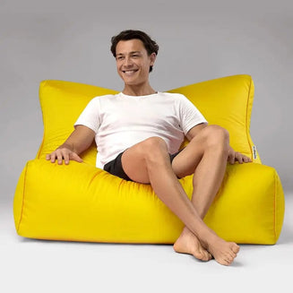 Man sitting on a yellow bean bag chair against a gray background