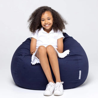 Young girl sitting on a navy bean bag chair against a white background