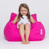 Young girl sitting on a bright pink bean bag chair against a white background
