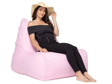 Woman sitting on a pink bean bag chair wearing a black outfit and beige hat.