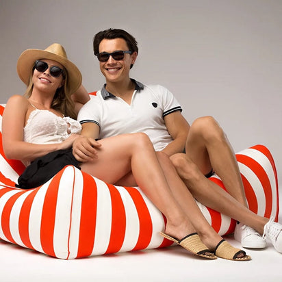 Two people sitting on a red and white striped bean bag chair against a gray background.