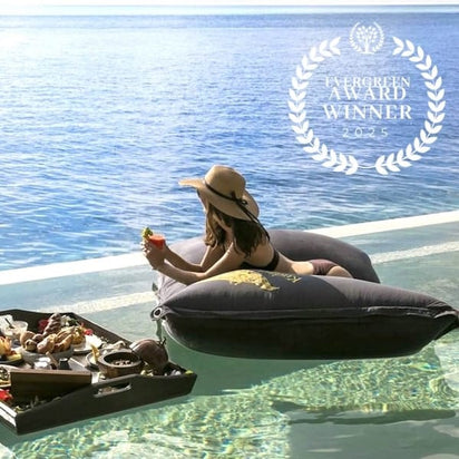 Woman relaxing on a floating pillow by the pool with a scenic view of water.