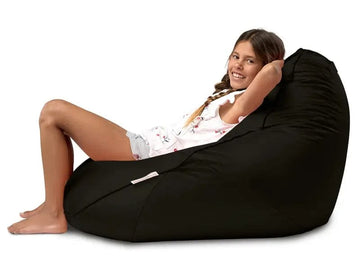 Young girl sitting on a black bean bag chair against a white background