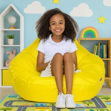 Child sitting on a yellow bean bag chair in a colorful room with shelves and toys.