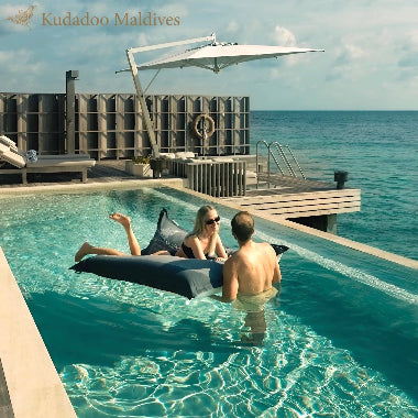Two people relaxing in a pool with ocean view at Kudadoo Maldives.