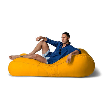 Man sitting on a large yellow bean bag sun lounge against a white background