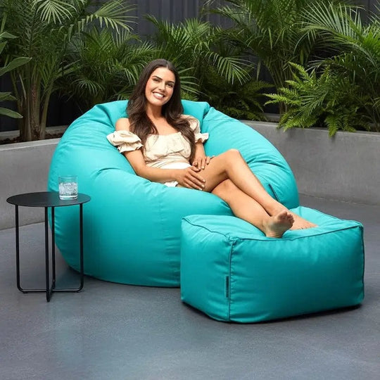 Woman sitting on a large turquoise bean bag chair outdoors with plants in the background